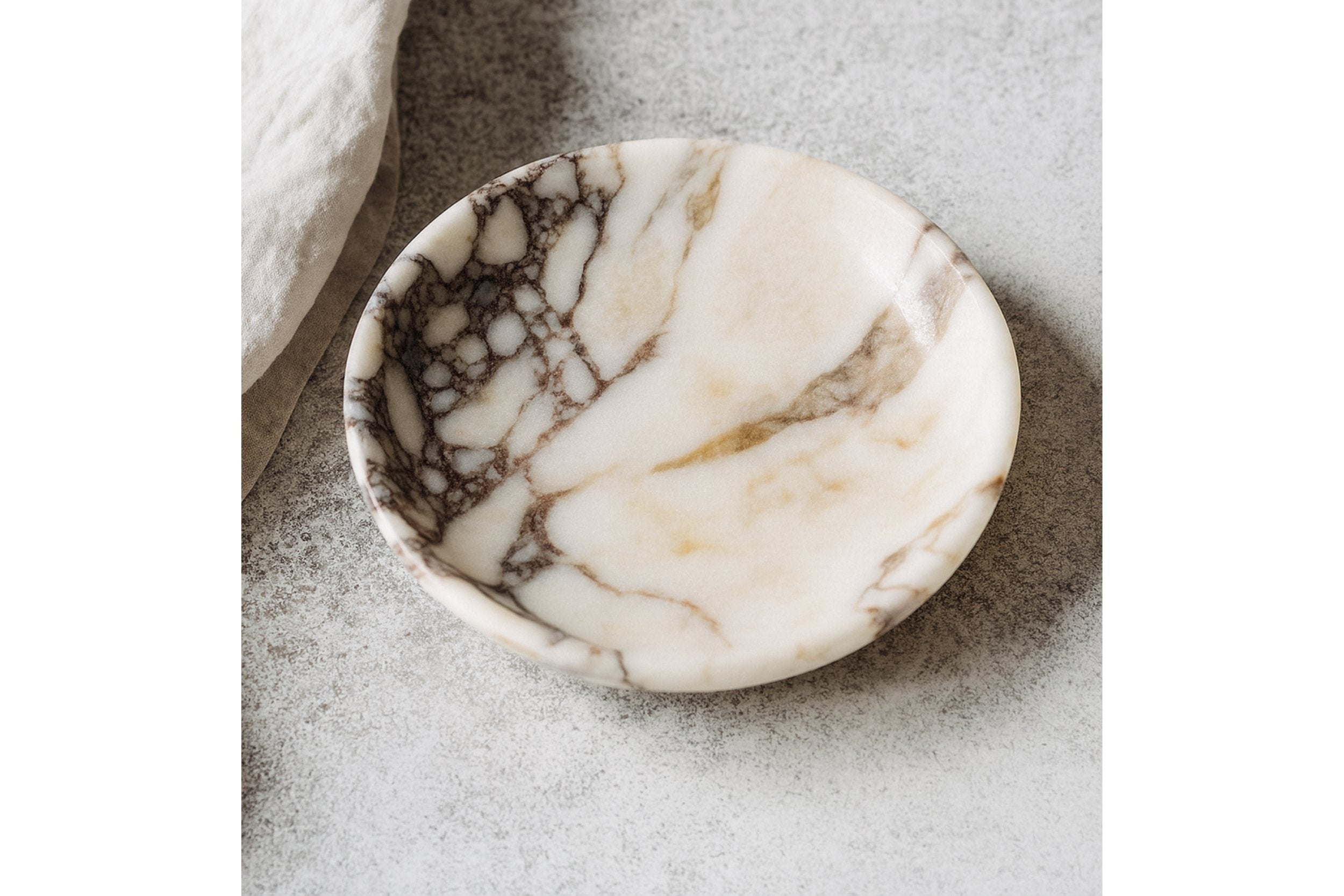 Calacatta Viola marble plate styled in a refined interior scene with linen fabric and soft lighting, evoking modern luxury.