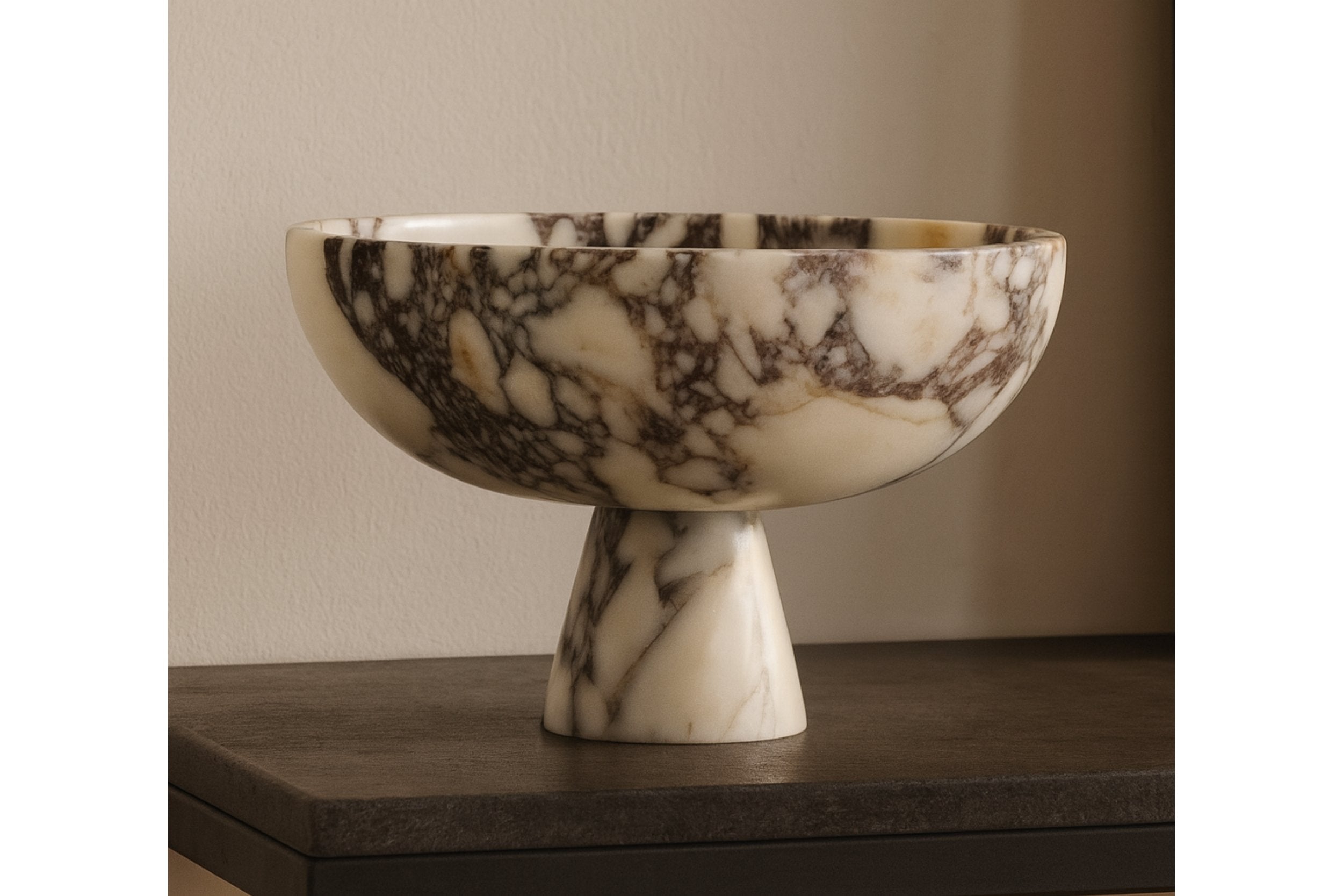 calacatta viola marble pedestal bowl styled on neutral shelf with books and sculptures, modern interior soft daylight