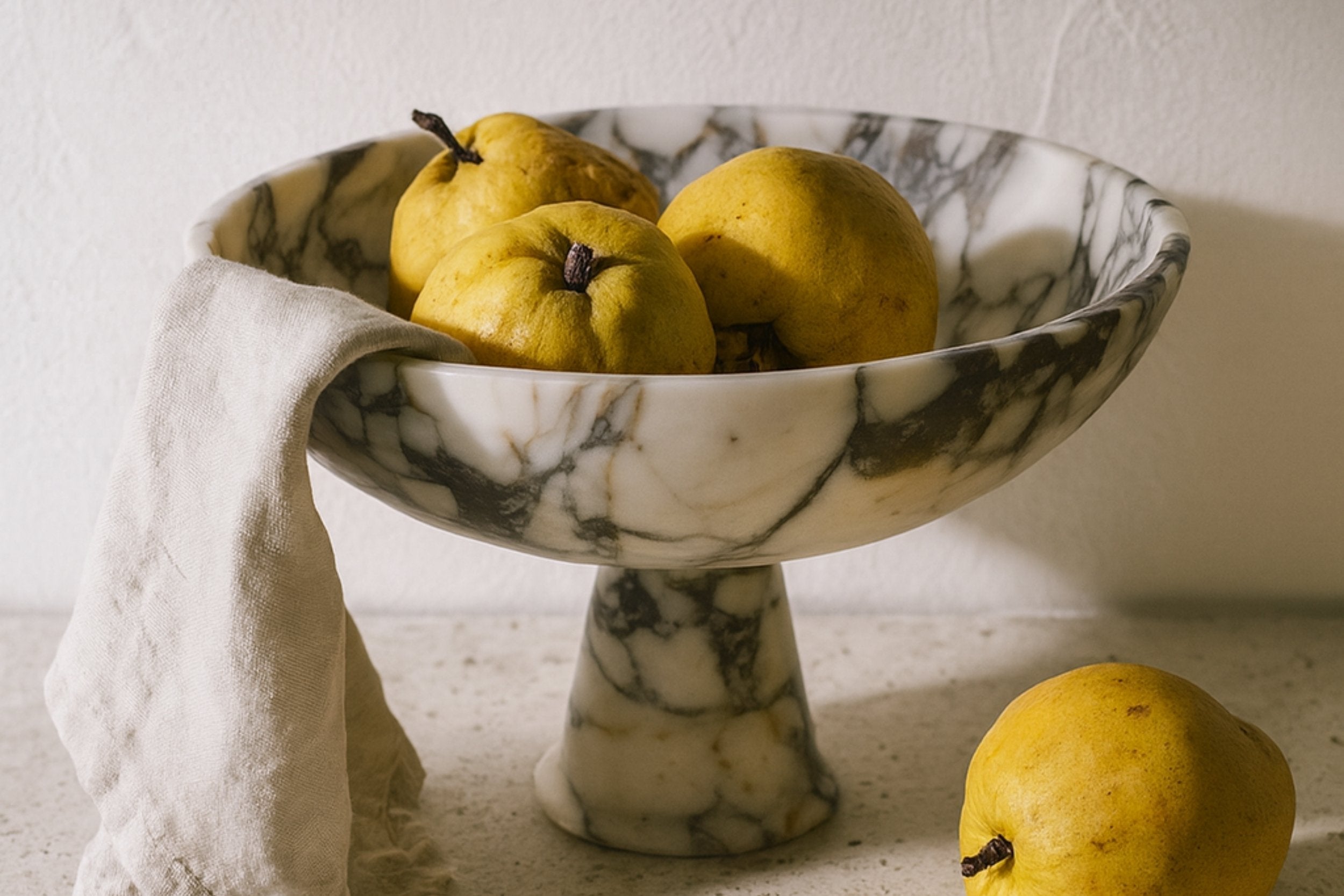 Calacatta Viola marble pedestal bowl styled with fruits and linen on neutral surface.