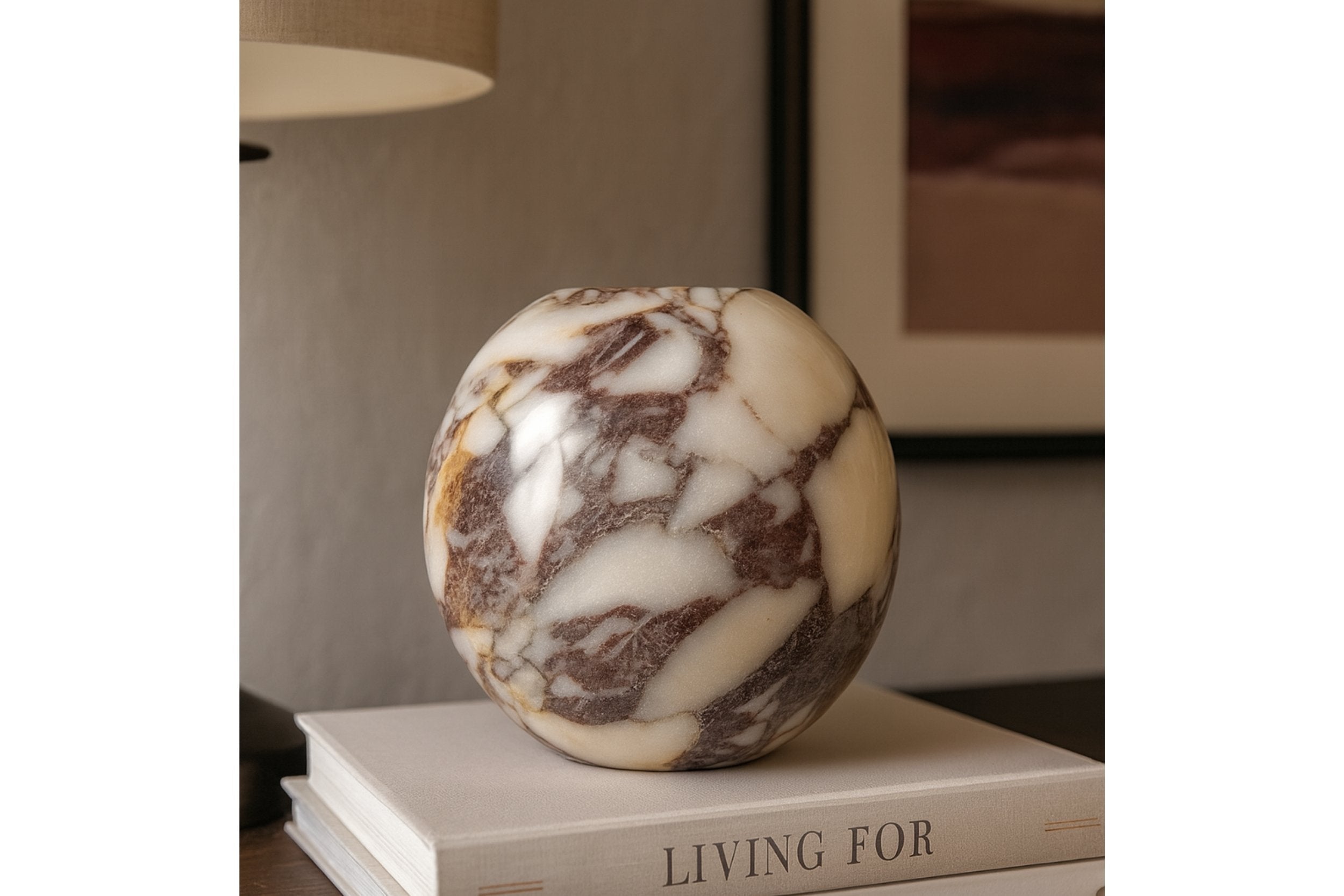 Round Calacatta Viola Marble Vase styled on coffee table books in a modern interior, warm lighting and elegant home aesthetic.
