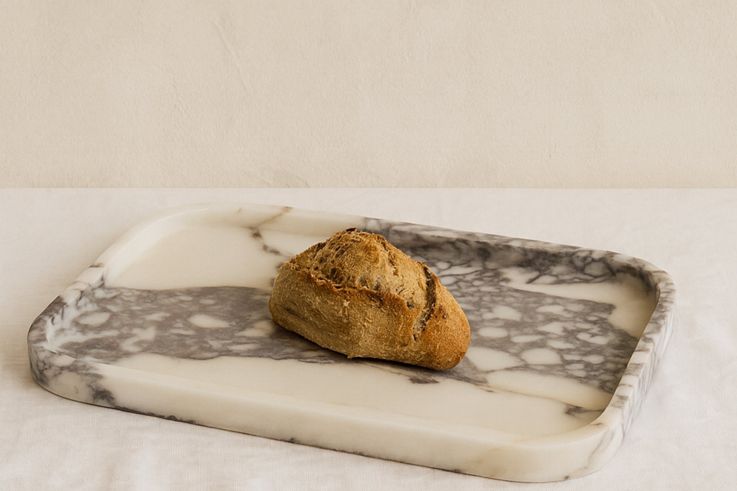Calacatta Viola marble tray styled on a linen surface with rustic bread, soft daylight.