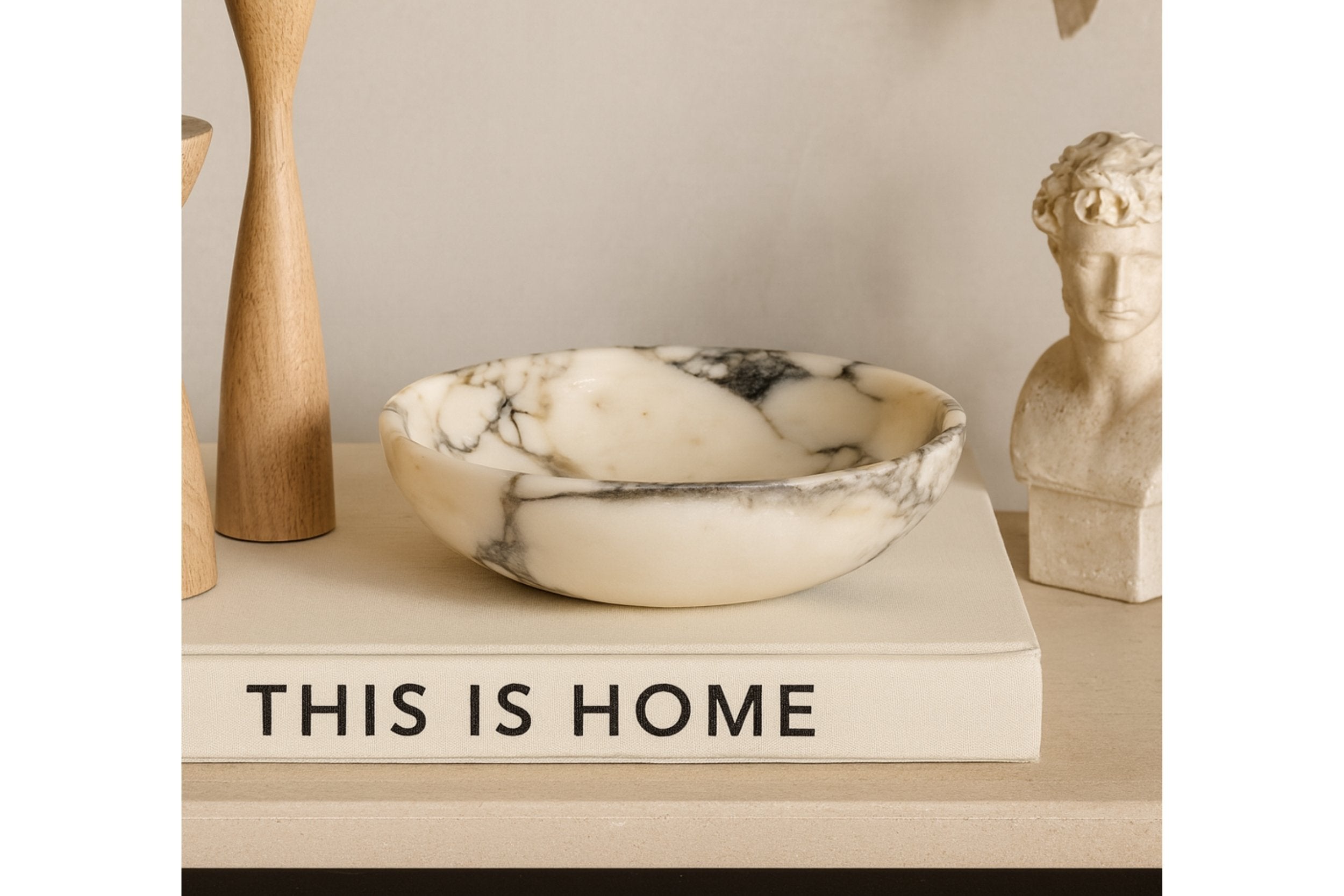 Calacatta Viola marble bowl displayed with wooden and sculptural decor objects, warm architectural lighting and calm tone.
