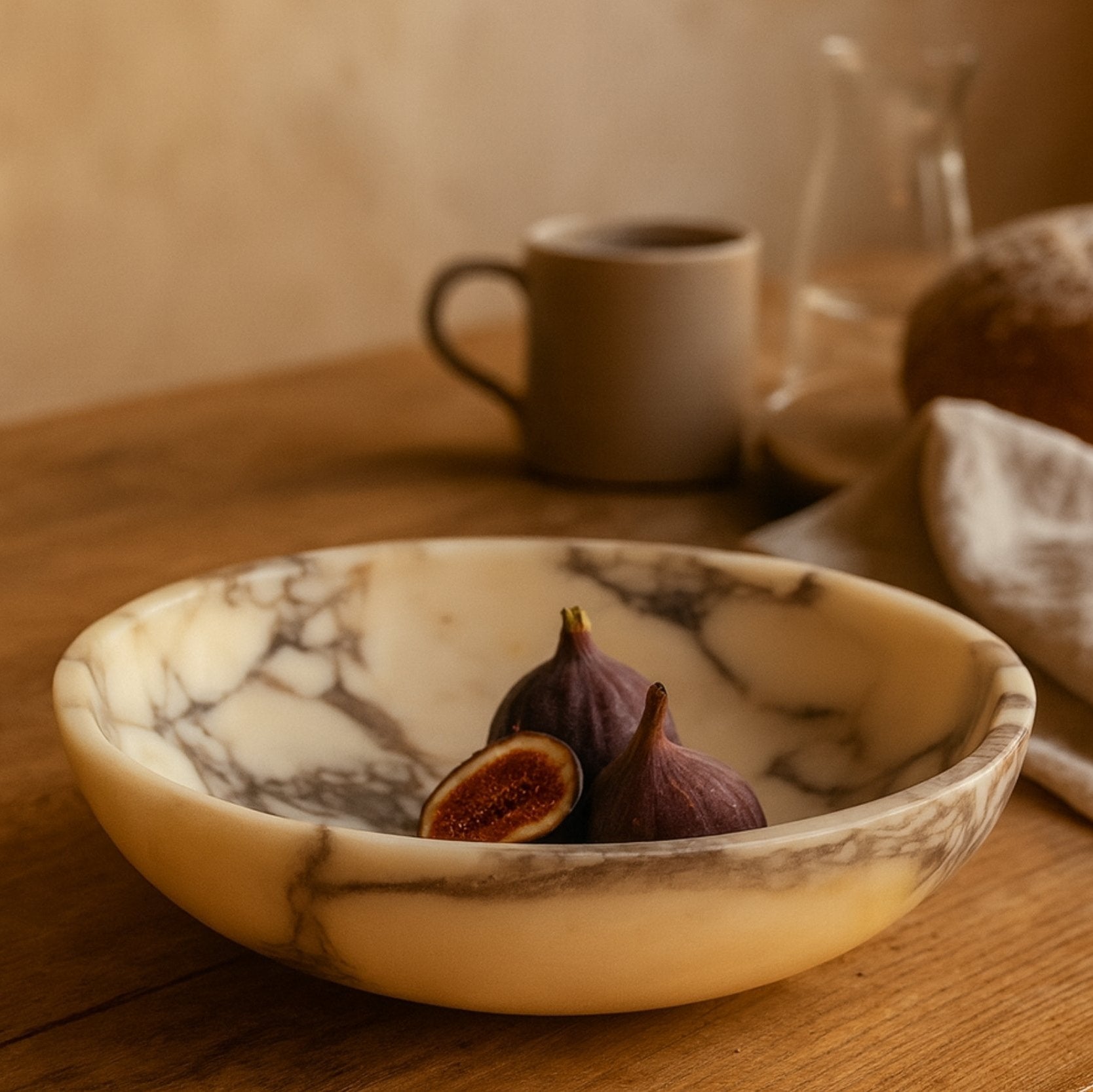 Calacatta Viola marble bowl with figs on wooden table in warm natural light, evoking cozy luxury and artisanal elegance.