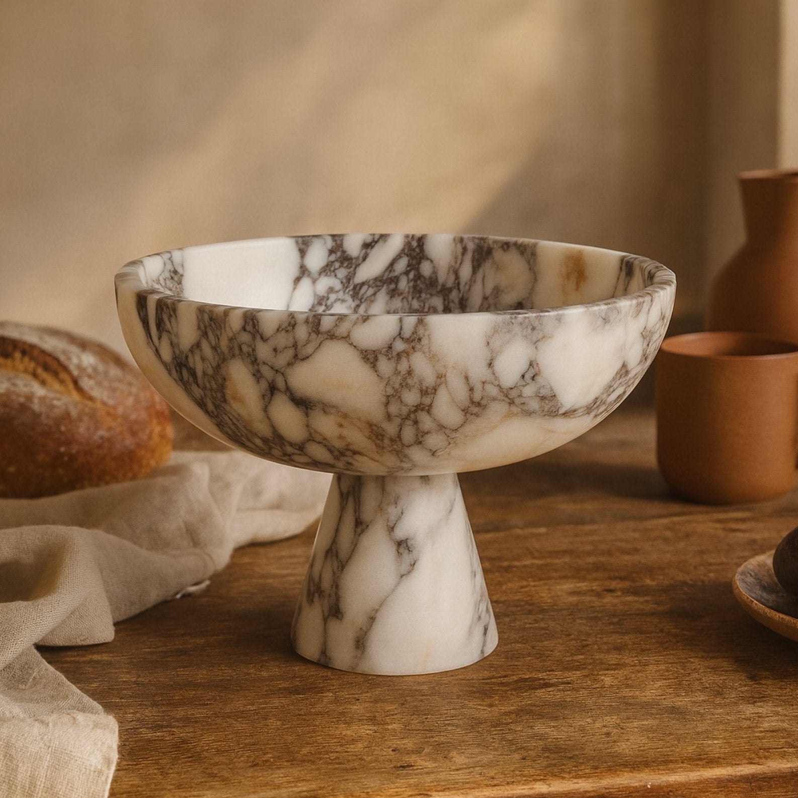handmade calacatta viola marble footed bowl on wooden table with olive branch and warm earthy tones