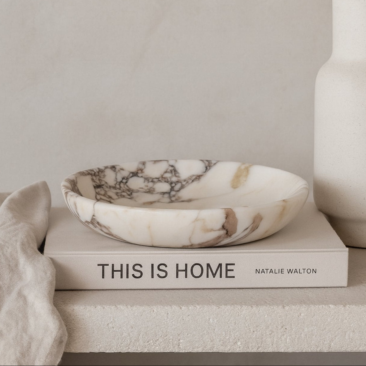 Minimalist scene featuring Calacatta Viola marble plate on neutral books with soft shadows and natural dried florals.