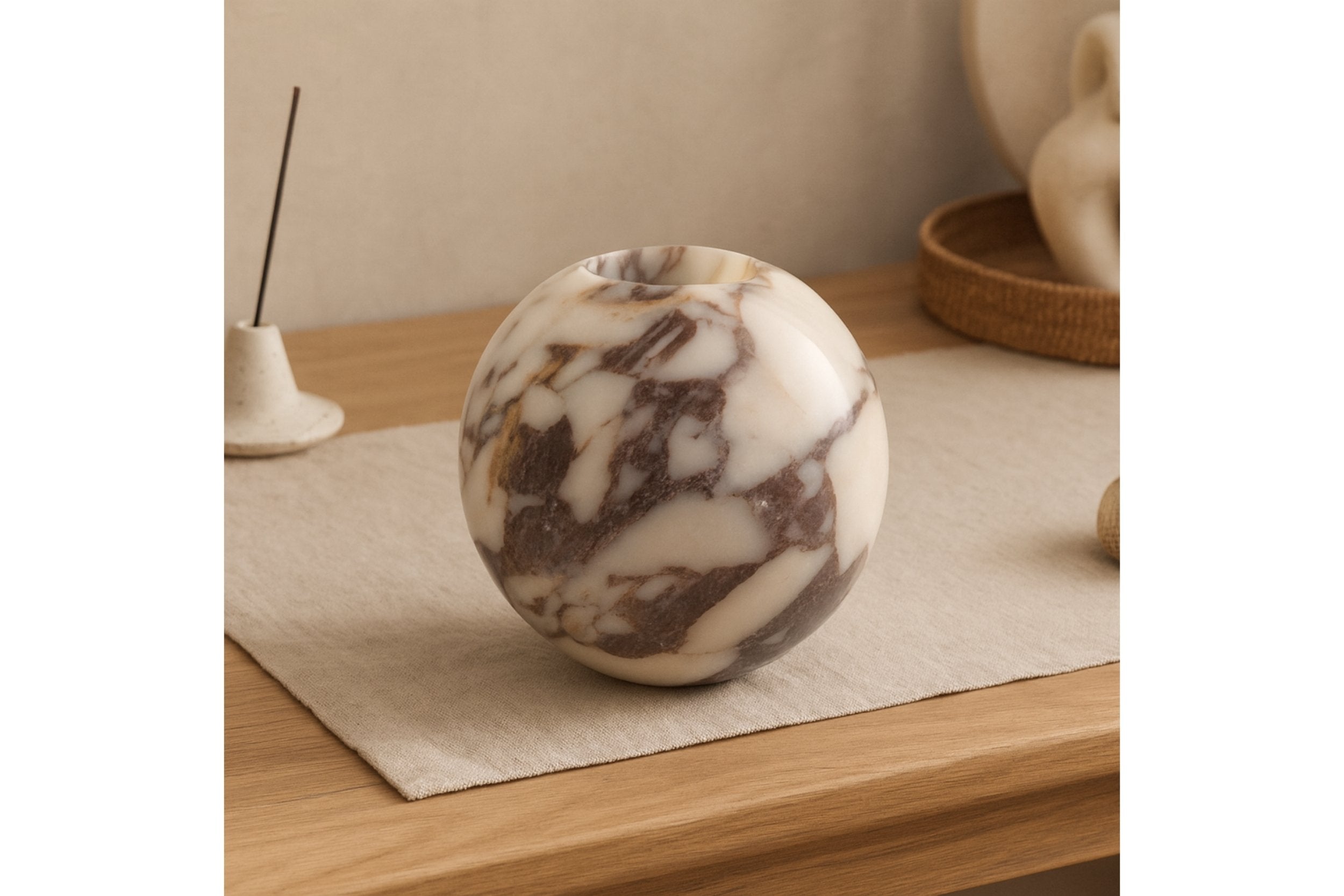 Sculptural Calacatta Viola marble vase on linen mat with soft beige background, styled with modern organic home accessories.