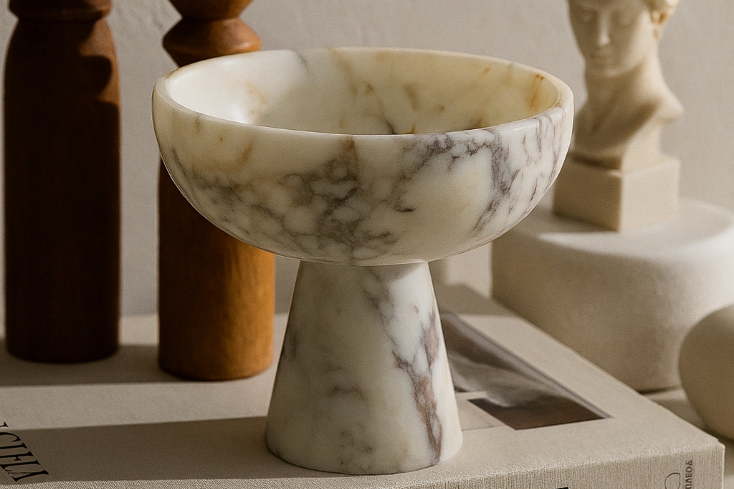 Calacatta Viola marble pedestal bowl styled on “This is Home” book with warm natural lighting and classic decor elements.