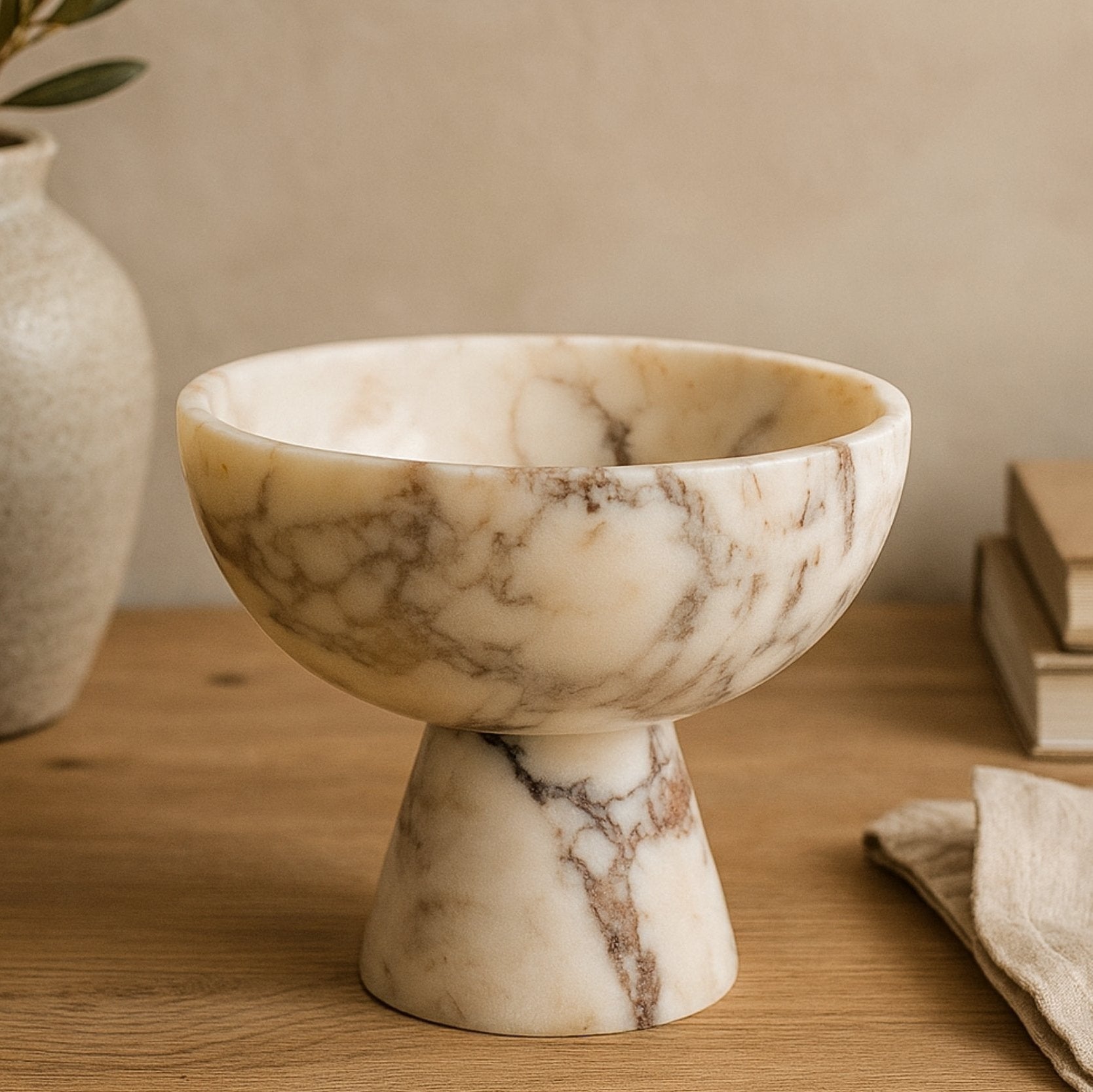 Handmade Calacatta Viola marble bowl on wooden table with olive branch vase and neutral home decor setup.