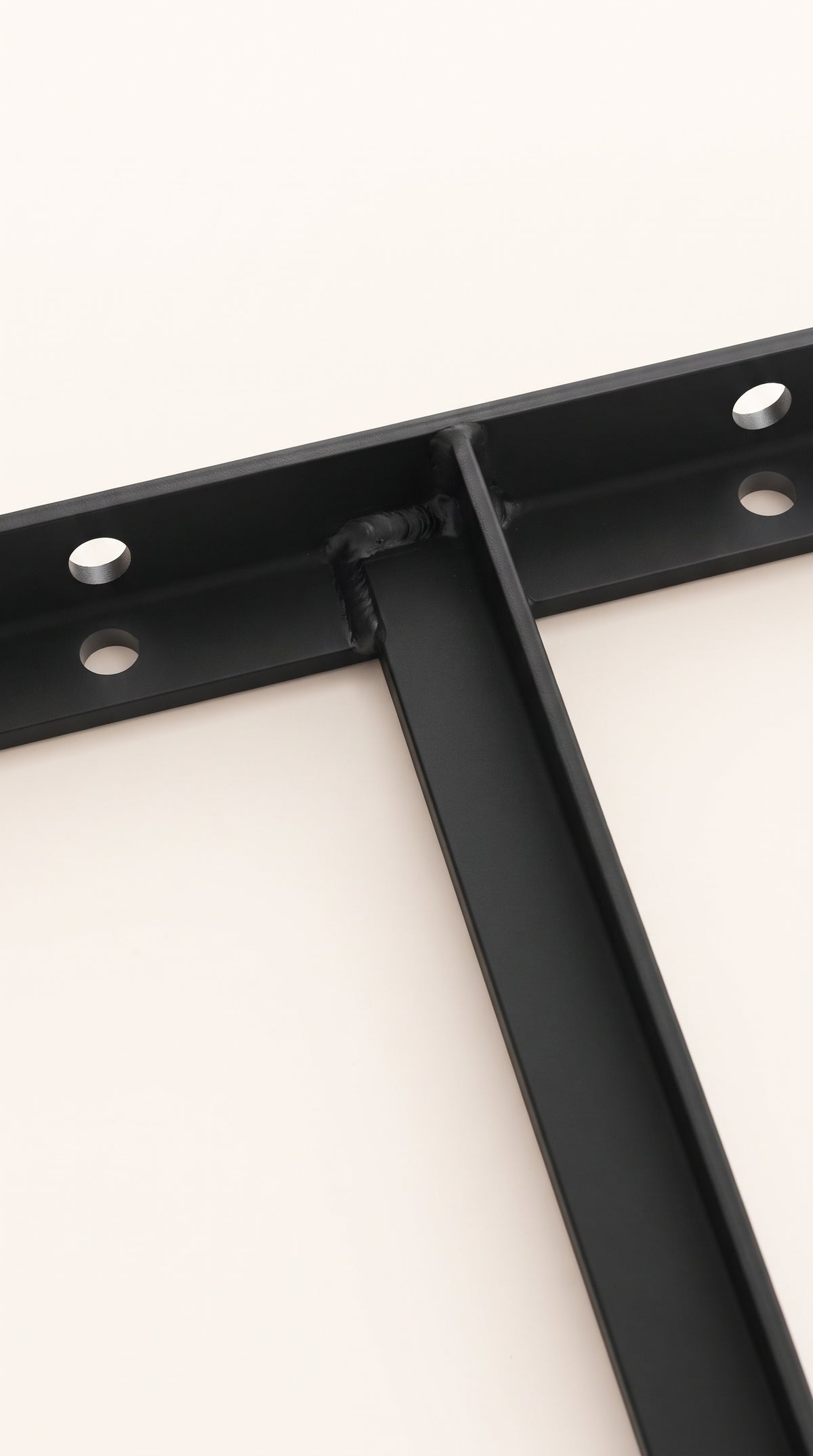 Close-up of the welded connection between the black metal bracket arm and mounting crosspiece, with circular mounting holes.