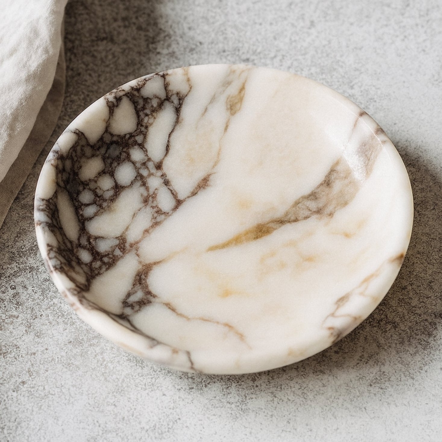 Calacatta Viola marble plate styled in a refined interior scene with linen fabric and soft lighting, evoking modern luxury.