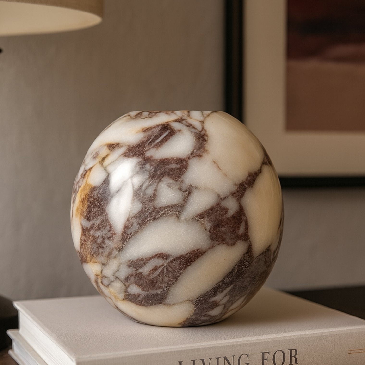 Round Calacatta Viola Marble Vase styled on coffee table books in a modern interior, warm lighting and elegant home aesthetic.