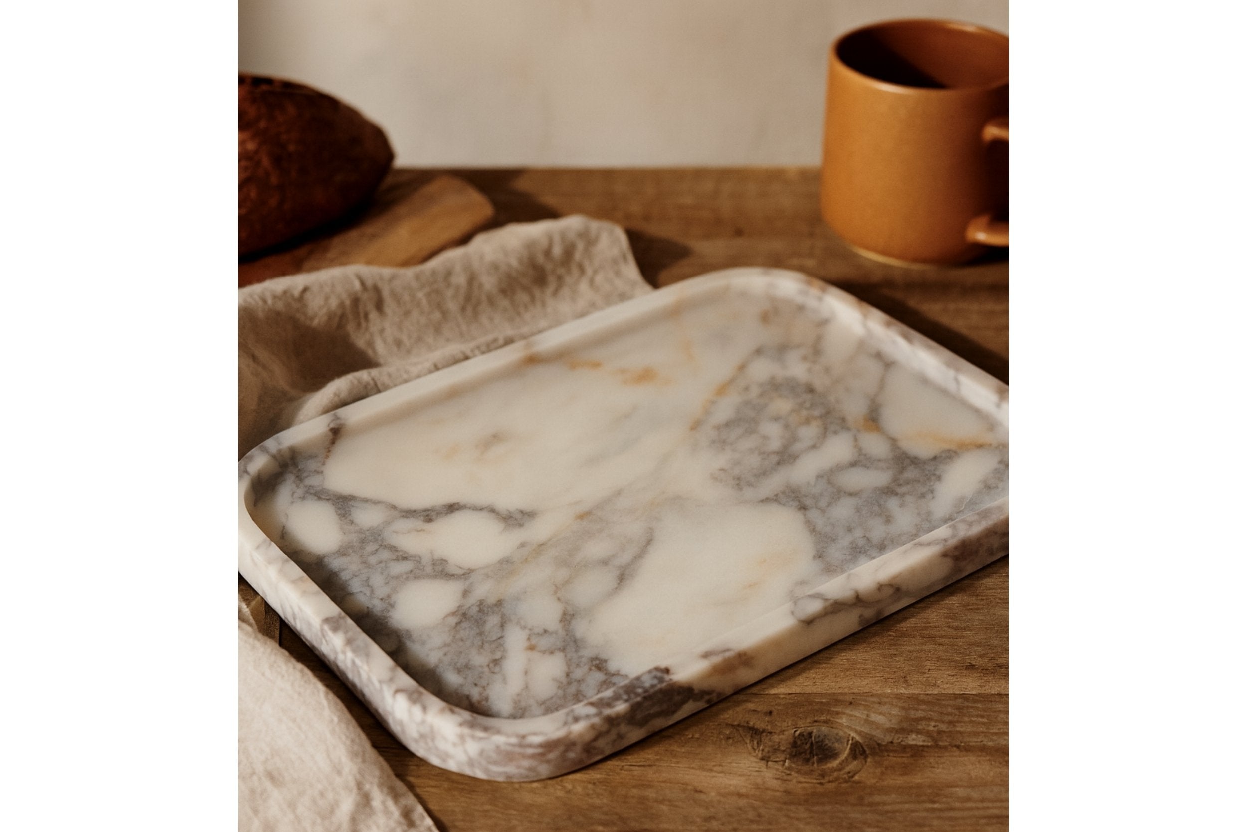 Calacatta Viola marble tray on a rustic wooden table with warm light and ceramic cup for home serving inspiration