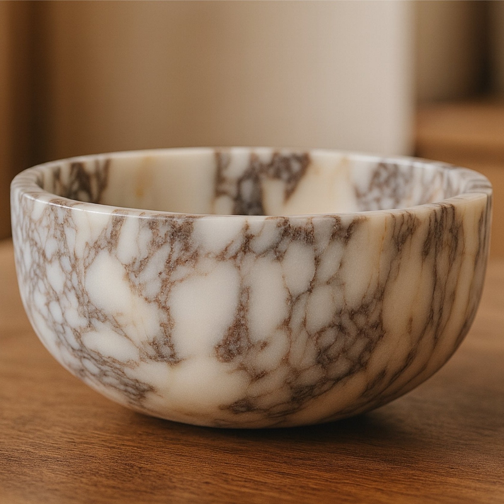 Handcrafted Calacatta Viola marble bowl on warm wooden countertop in soft architectural lighting.
