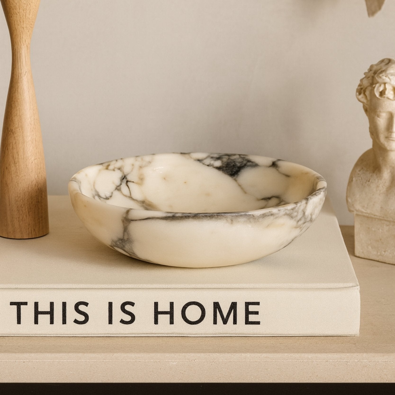 Calacatta Viola marble bowl displayed with wooden and sculptural decor objects, warm architectural lighting and calm tone.