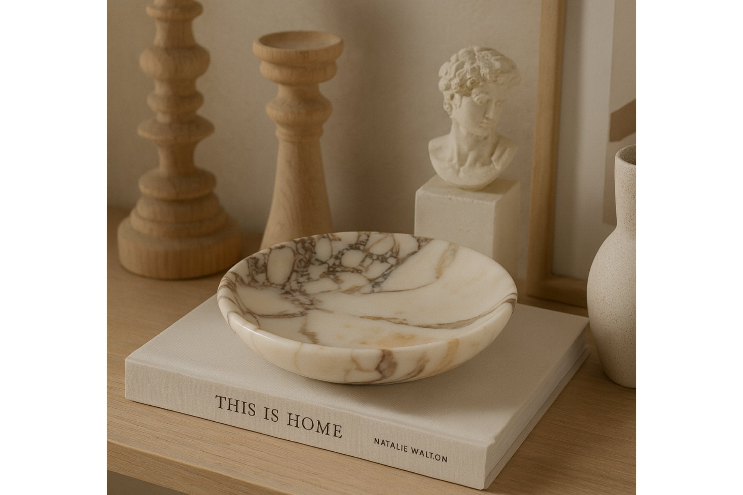 Calacatta Viola marble plate on “This Is Home” book surrounded by wooden candlesticks and art sculpture, reflecting timeless elegance.