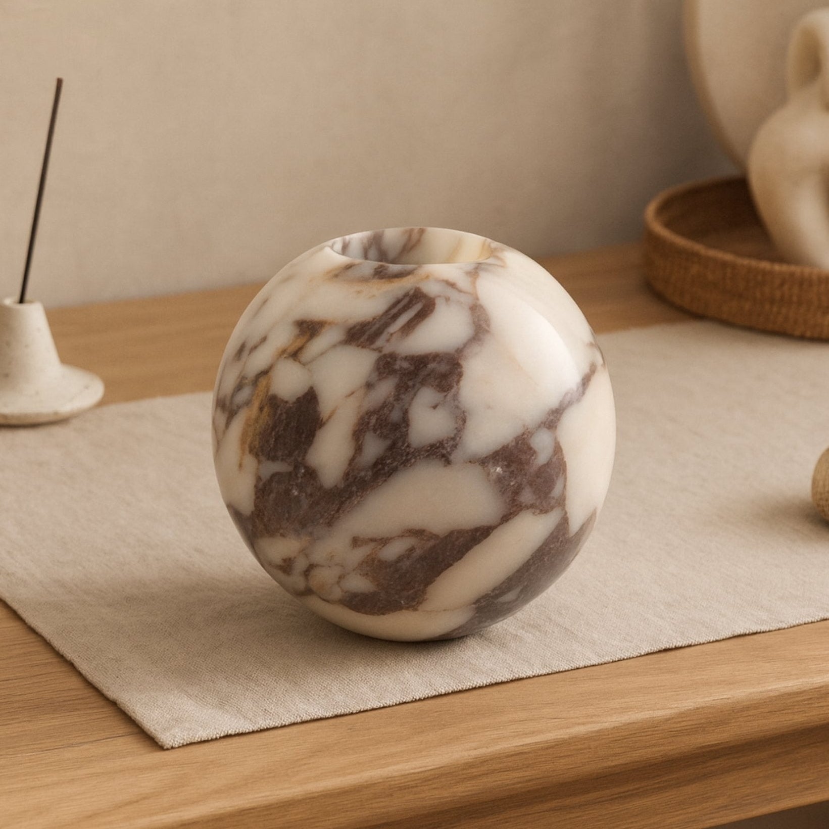 Sculptural Calacatta Viola marble vase on linen mat with soft beige background, styled with modern organic home accessories.