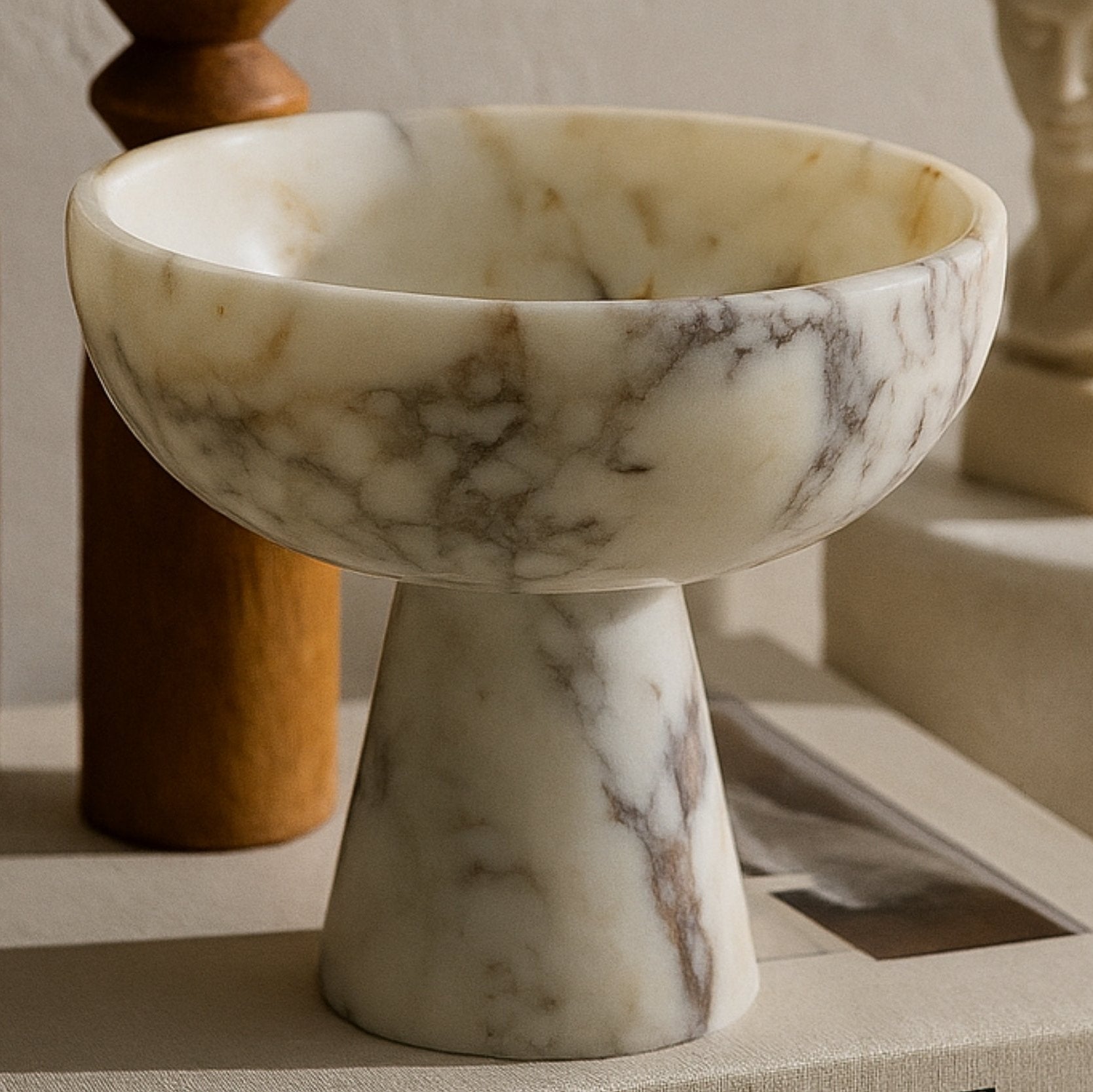 Calacatta Viola marble pedestal bowl styled on “This is Home” book with warm natural lighting and classic decor elements.