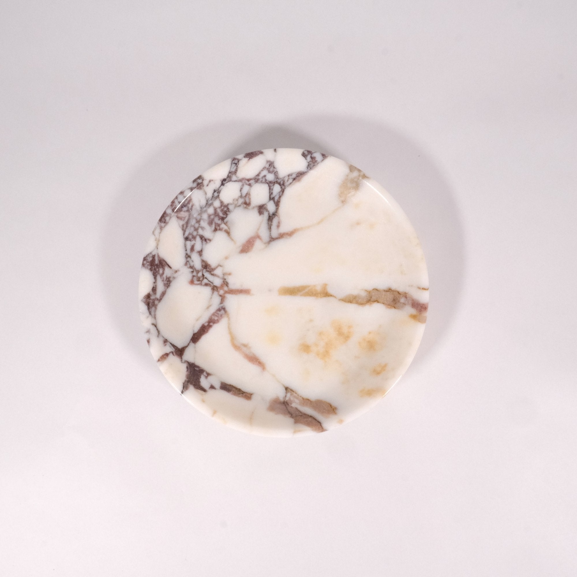 Top-down view of Calacatta Viola marble plate highlighting natural violet veining and circular form on minimalist beige backdrop.