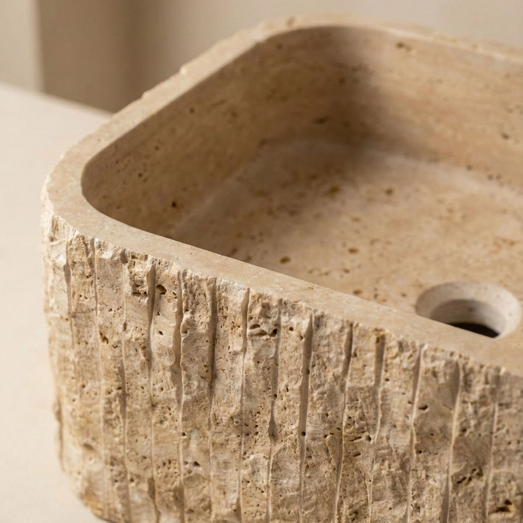 Close-up of fluted travertine sink edge showing hand-carved stone texture and natural pores