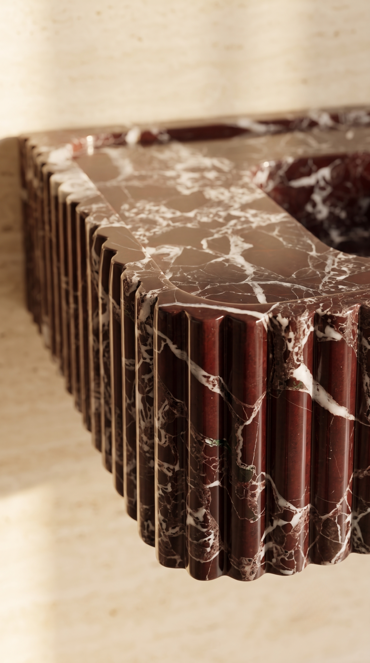 Close-up of handcrafted fluted Rosso Levanto marble sink corner and natural veining
