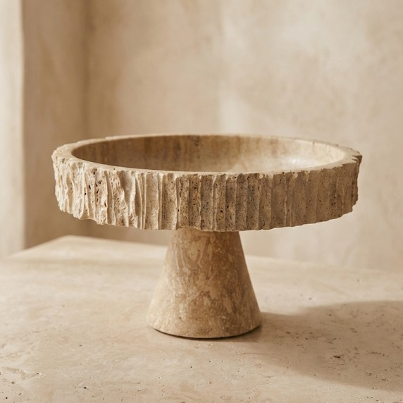 Travertine pedestal bowl with fluted edge on beige studio background
