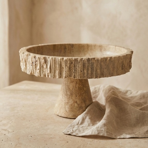 Fluted travertine bowl styled with neutral linen fabric
