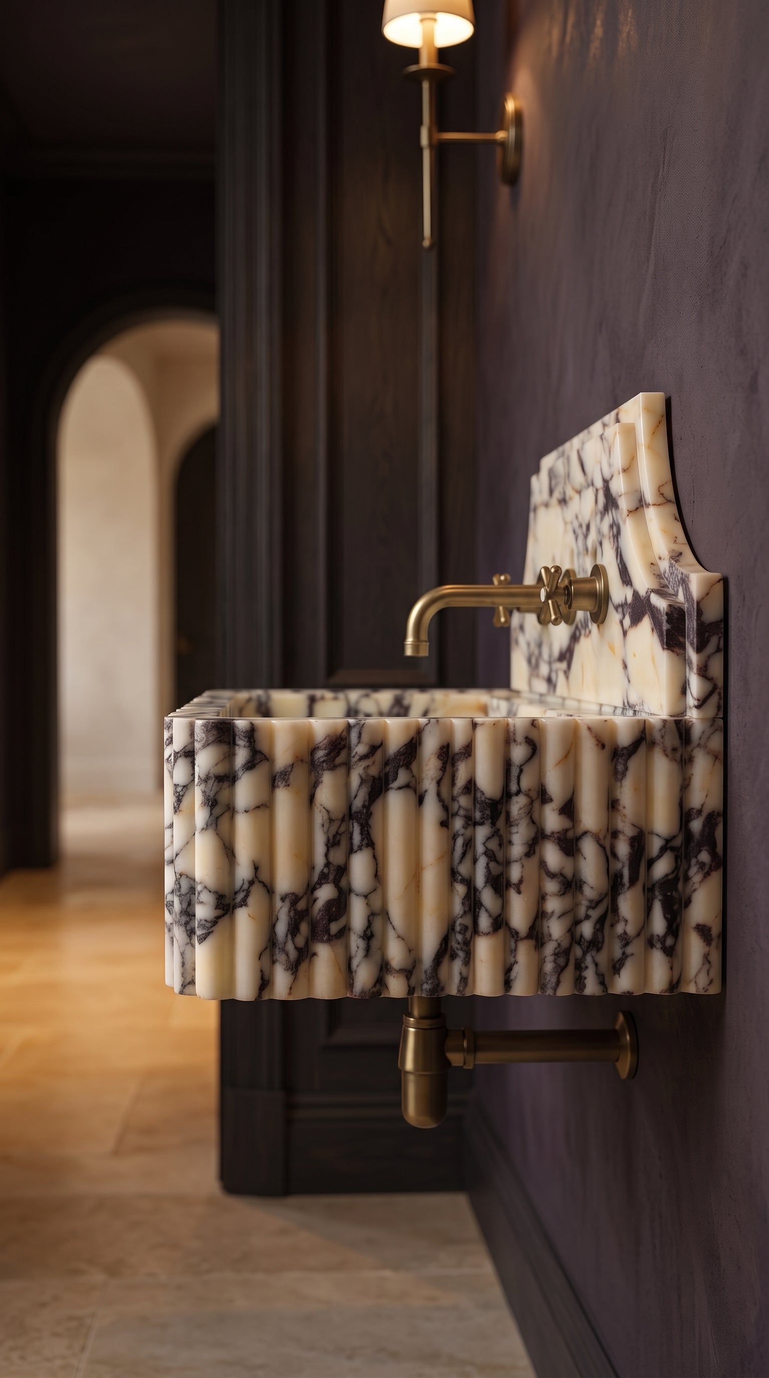 Side view of a fluted Calacatta Viola marble sink with brass faucet in an elegant boutique hotel powder room.