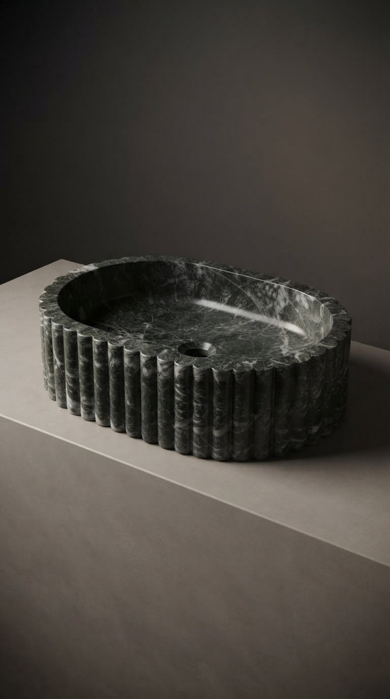 Dark oval marble vessel sink displayed on a pale stone plinth, highlighting its curved silhouette and carved vertical fluting.