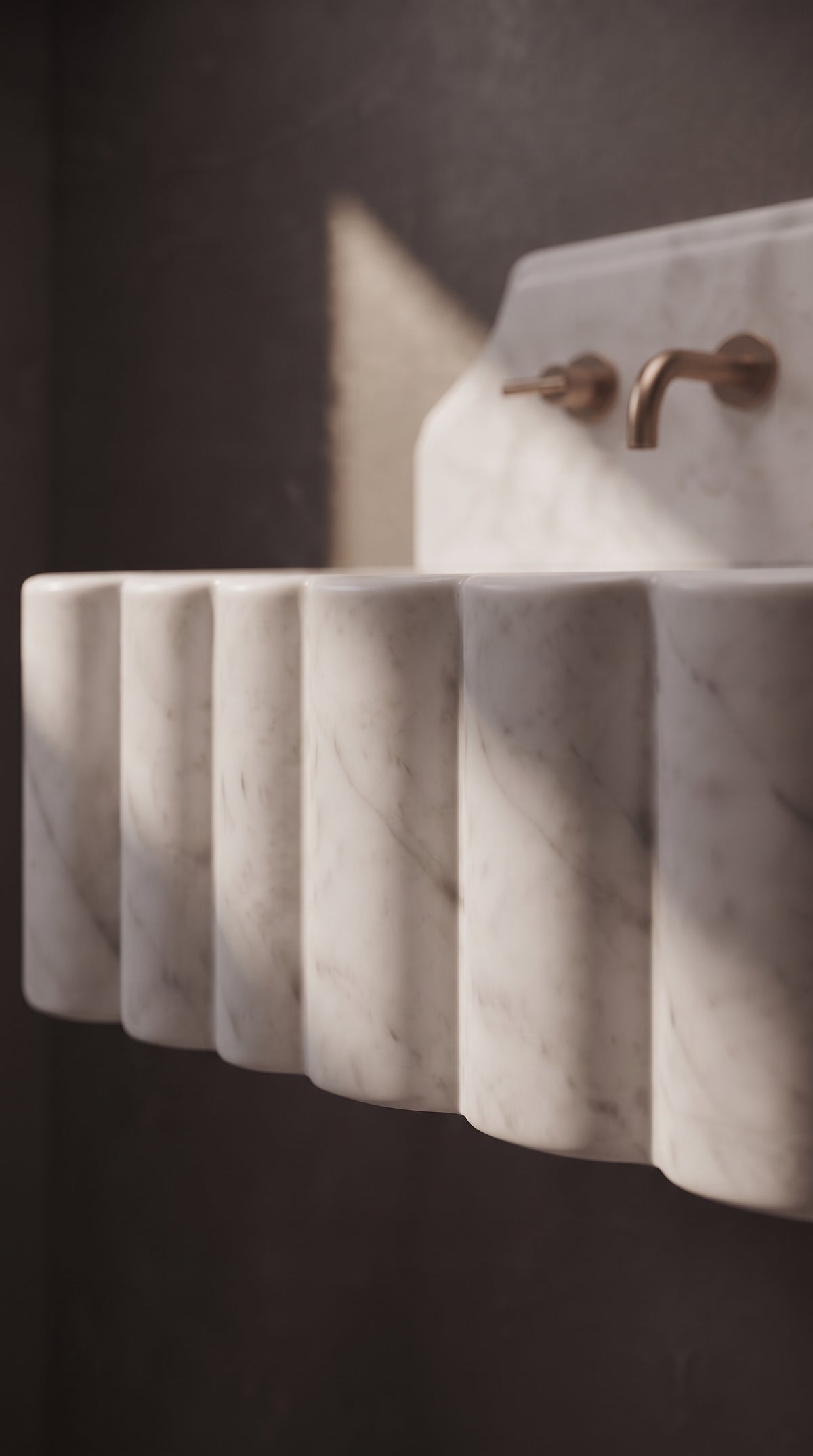 Artistic close-up of rounded scalloped marble detailing illuminated by soft directional light on a Muğla White bathroom sink.
